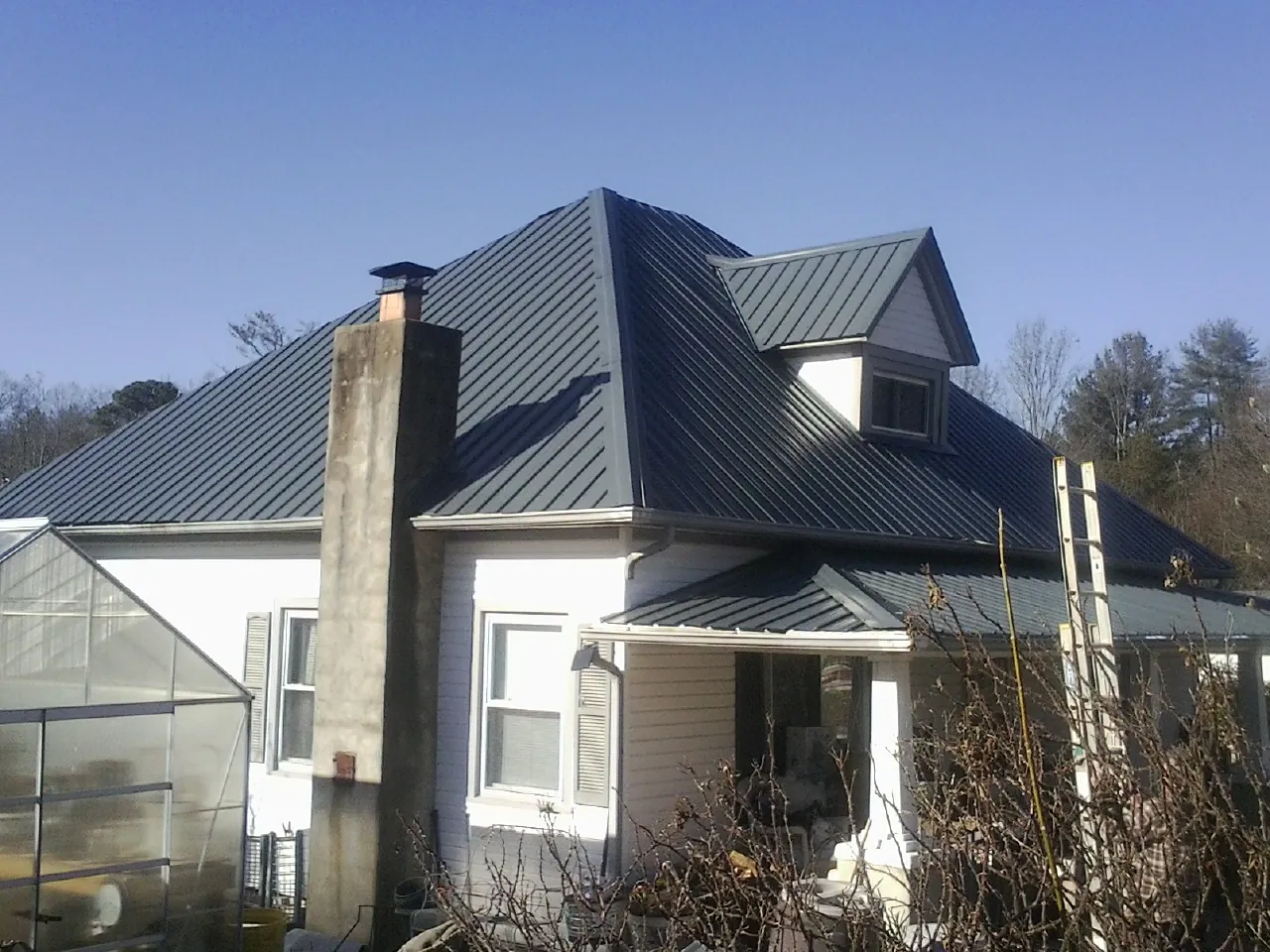 Dark blue standing seam metal roof on a white farmhouse with dormer — Slate & Tile Roof Repair by Roofing Brothers in Gainesboro
