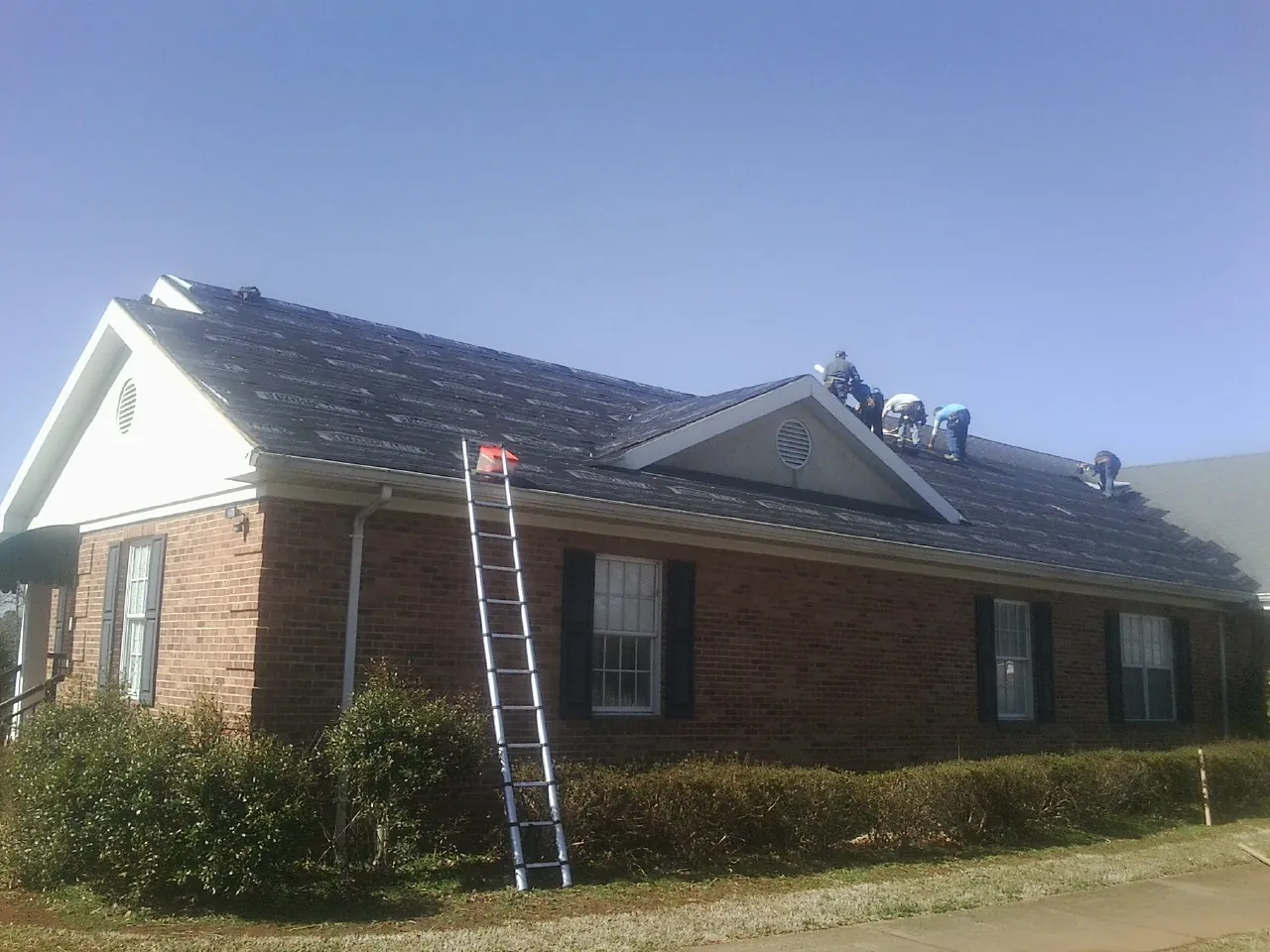 Crew tearing shingles off a brick ranch roof with a ladder set — Metal Roof Repair work by our crew in Gainesboro