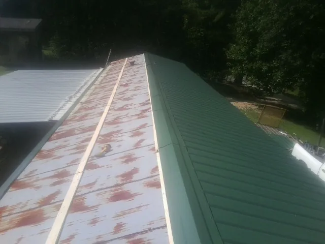 Old rusted panels beside newly installed green metal roofing — Wind Damage Roof Repair by Roofing Brothers in Gainesboro