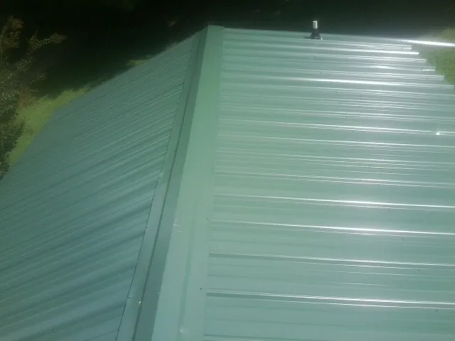 New green metal panels meeting at the ridge of a roof — Flat Roof Repair work by our crew in Gainesboro