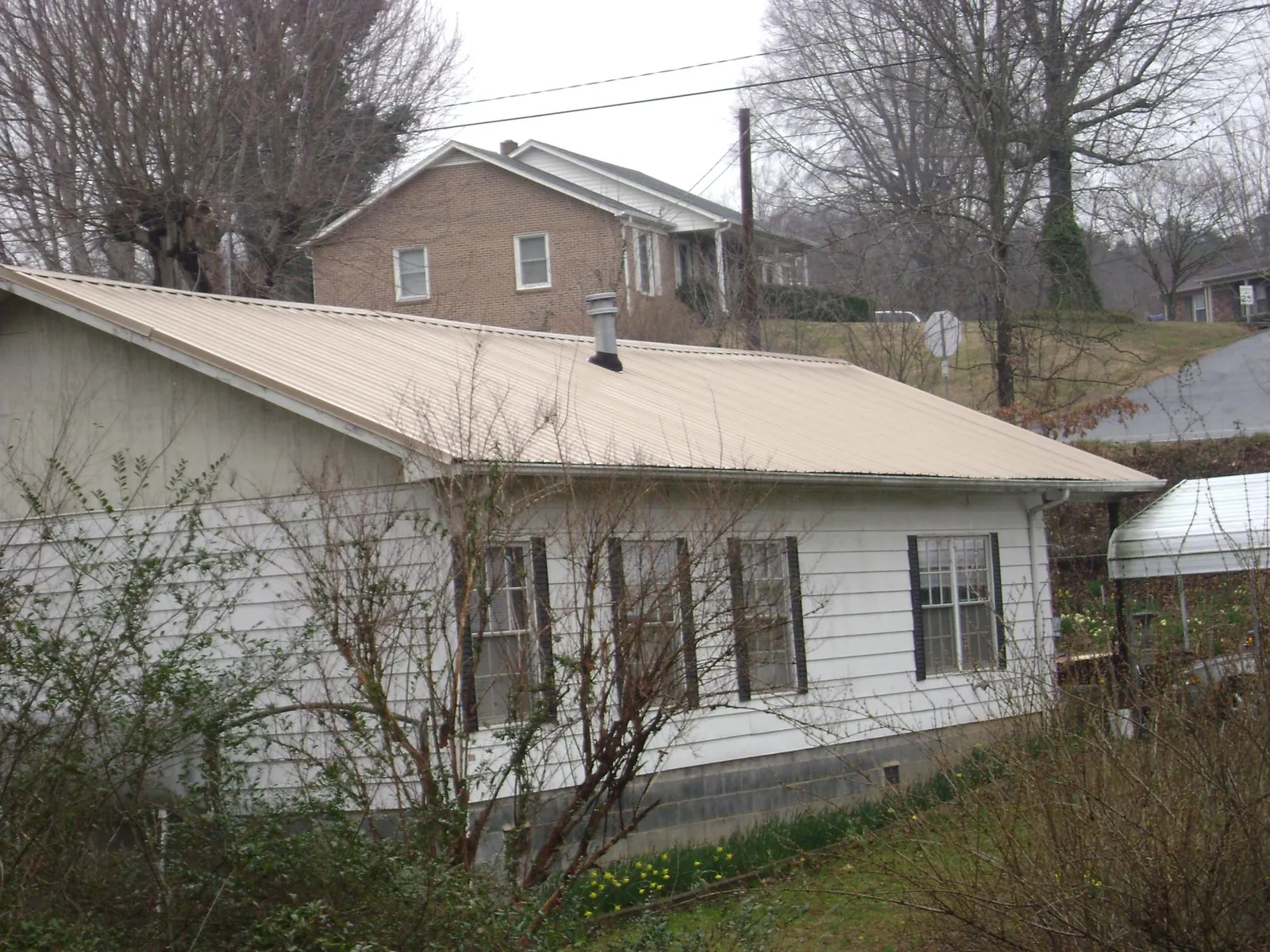 Tan metal roof on a white sided house set into a hillside — Commercial Roofing by Roofing Brothers in Gainesboro